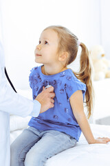 Fototapeta premium Doctor examining a little girl by stethoscope. Happy smiling child patient at usual medical inspection. Medicine and healthcare concepts