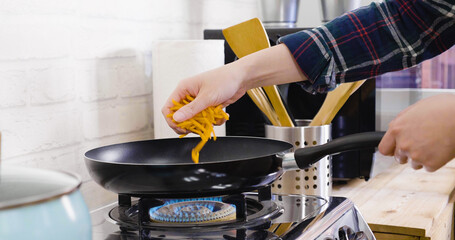 unrecognized asian woman hands holding lots of chopped carrots and puts into frying pan on gas...