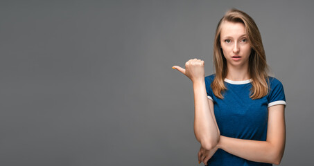 Young woman over isolated gray background pointing finger to the side. Presenting your product. Expressive facial