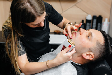 Obraz na płótnie Canvas A professional stylist in a modern stylish barbershop shaves and cuts a young man's hair. Beauty salon, hair salon