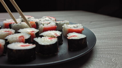 Smooth hit on a plate with Japanese food. Female hand with chopsticks takes sushi from a plate.Sushi rolls japanese food rotated over black background. California Sushi roll with tuna, vegetables