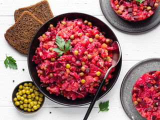 Vinaigrette. Traditional russian beetroot salad with boiled vegetables, pickled cucumbers, sour cabbage, olive oil and green canned peas. Vegetarian healthy dinner. White wooden background. Top view.