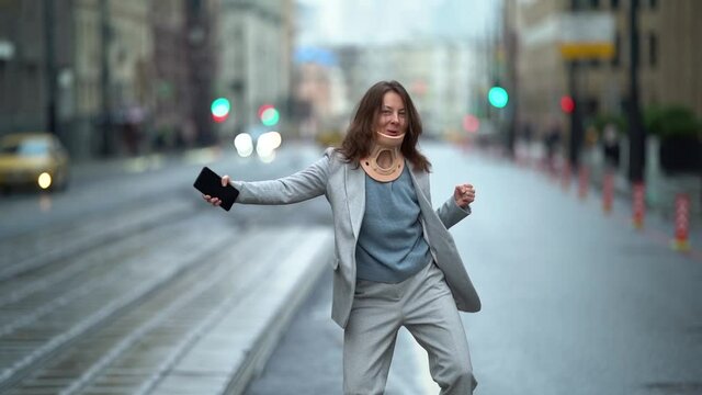 Cheerful lady in a neck collar injured spine dancing on the road in the city and waving her hands like a madwoman