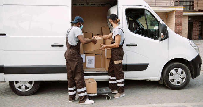 Portrait of African American and caucasian delivery men in mask and uniform in front of his van. Couriers Delivers Parcel to client