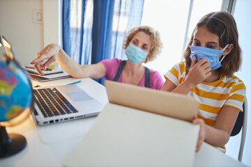 Child home studying education, homeschooling, with private tutor / mother with protective mask in the time of viruses, flu and seasonal pandemic.