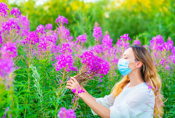 A girl in a medical mask stands against a background of greenery and sniffs a bouquet of flowers. Allergy symptoms. Walking during quarantine