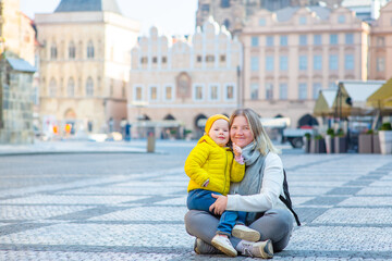 Mom sit with a little daughter sitting on a deserted old town square in Prague