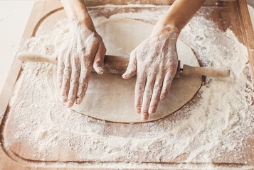 Woman baking bread or pizza dough with rolling pin on wooden table