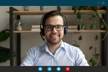 Head shot portrait screen view smiling employee wearing headset consulting client online, looking...