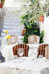 Outdoor restaurant in Italy. Empty glasses set in cafe with beautiful italian street at the background. Food, travel and vacation concept.