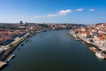 Beautiful view of the banks of the Douro river in the city of Porto. A hill descending to the water with many colorful houses. Lots of cafes on the waterfront and wooden traditional boats at the pier.