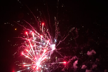 Fototapeta premium On a black background, red rays and sparks of a scattering fireworks with smoke.