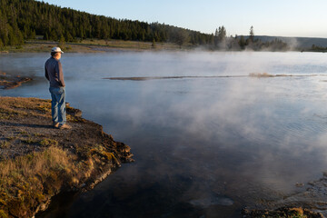 Fototapeta na wymiar Lone visitor standing on the shore of a thermal lake watching the steam rising, Fire Hole Lake, Yellowstone NP, Wyoming