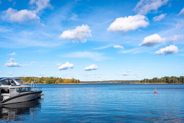 Fototapeta premium Autumn landscape of the coast of Sweden. Forest islands with colorful trees in the gulf of the Baltic Sea. The yacht boat moored to the shore. Panoramic view of Scandinavia in an autumn day.