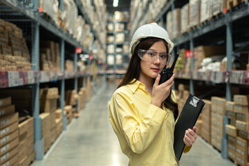 Female warehouse worker inspecting a warehouse in a factory. Wear a safety helmet and glasses for work safety. Concept of warehouse.