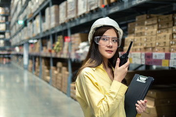 Female warehouse worker inspecting a warehouse in a factory. Wear a safety helmet and glasses for work safety. Concept of warehouse.