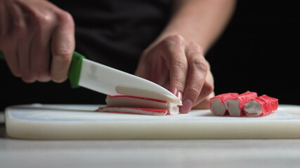 Female hands make salad of crab sticks cucumber corn eggs in the kitchen at home. Woman cuts crab sticks into salad