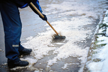 Worker breaking ice with hand ice breaker tool, cleaning ice with razor scraper on the sidewalk. Worker in uniform cleaning ice and snow with icebreaker tool. Janitor cleans area. Snow removal - obrazy, fototapety, plakaty