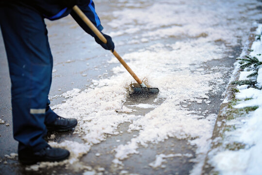 Worker breaking ice with hand ice breaker tool, cleaning ice with razor scraper on the sidewalk. Worker in uniform cleaning ice and snow with icebreaker tool. Janitor cleans area. Snow removal