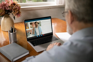 Rear view close up senior man watching webinar, learning language online, sitting at desk, young...
