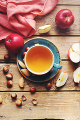Cozy morning autumn composition with cup of tea, fresh apples and nuts on rustic wooden table