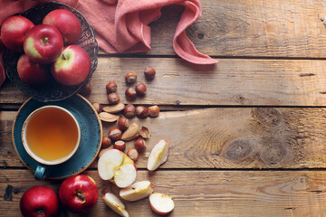 Cozy morning autumn composition with cup of tea, fresh apples and nuts on rustic wooden table