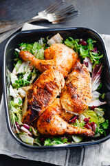 Top view of roasted chicken legs and breasts served with fresh salad and mushrooms in black pan.