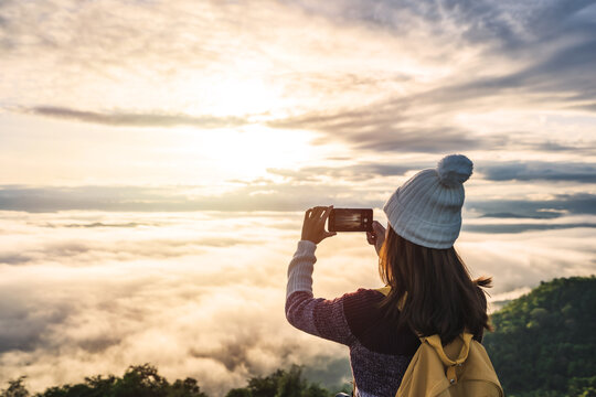 Young woman traveler using smart phone to taking a beautiful sunrise and the sea of mist on the mountain in the morning, Travel lifestyle concept