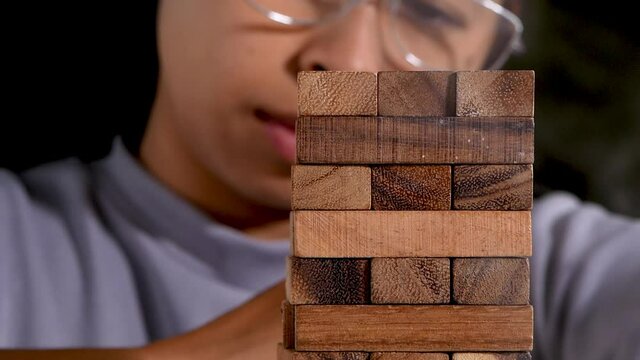 Woman thinking and concentrating on pulling out a wooden blocks in room alone. Jenga falls on the table. Concept of success and failure in the business.