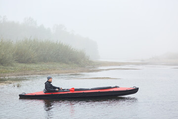 Man paddling canoe on cold day in lake, having rest in active way, sitting in boat and looking at beautiful nature, wearing jacket and cap, water sport.