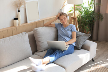 Smiling young woman with headphones and laptop on the sofa.