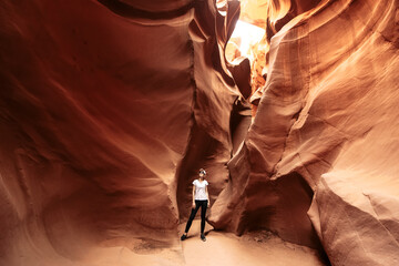 A young woman is walking on path between bizarre rocks in incredible Antelope Canyon, Arizona, USA. - Powered by Adobe