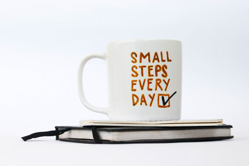 coffee mug with motivational writing "small steps every day" on notebooks and white background
