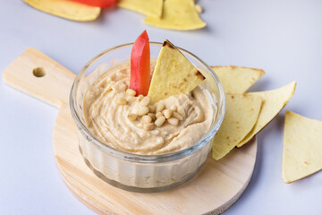 Glass Bowl of Hummus Chickpea Dip Nuts Paprika and Olive Oil With Pita or Chips on a Wooden Tray Blue Background Horizontal