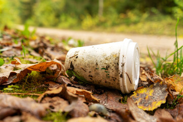 Old disposable coffee cup in the forest next to the road. Plastic recycling, pollution and global warming theme. Take away food industries impact on the environments. 