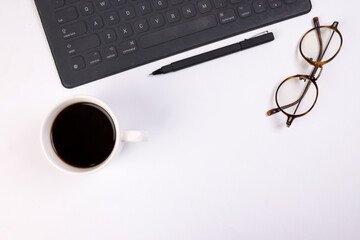 Black computer keyboard eyeglass coffee cup pen on white background top view copy text space