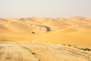 An empty asphalt road zigzagging through the desert and sand dunes in the United Arab Emirates