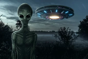 Fotobehang UFO Groene alien met zwarte grote glazen ogen op de achtergrond van een vliegende schotel. UFO-concept, buitenaardse wezens, contact met buitenaardse beschaving
