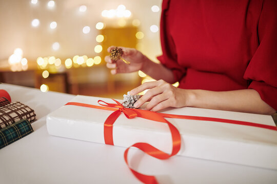 Close-up image of young woman decorating Christmas present with pine cones