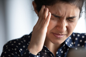 Closeup view frown face of indian woman feeling strong headache touch temple to reduce severe pain, suffering from panic attack in office, migraine overworked person or hangover alcohol abuse concept