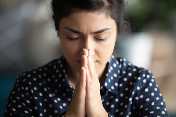 Fototapeta na wymiar Close up image religious young indian female closed eyes praying silently with palms folded together in front of face. Believing woman ask God for miracle, morning pray, faith and superstition concept