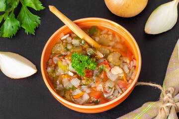 Fresh vegetable soup with onions, celery and tomatoes in dish on a black background. Healthy vegan (vegetarian) food. Top view