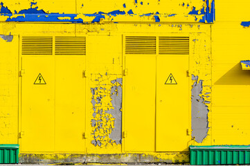 Doors leading to the technical rooms on the facade of the building with peeling yellow paint and visible spots of blue paint.