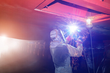 Industrial worker welding close up spark light for ship repair overhead position welding in shipyard under water ballast tank.
