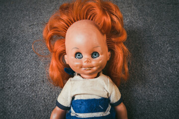 An old children's doll for girls with a gray background behind. A children's toy from the time of the communist system in Eastern Europe. Old plastic female doll. The concept of old children's toys