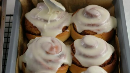 Pouring frosting on Freshly baked cinnamon rolls or Cinnabon close up. Sweet cream cheese frosting pouring on cinnamon rolls. Production of cinnamon rolls. Bakery products. Appetizing cinnamon buns