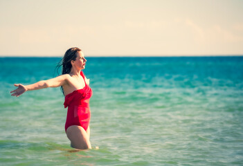 A young slender, beautiful European middle-aged woman is swimming in the sea, a mature brunette in a red bathing suit is enjoying her summer vacation. Freedom and cheerfulness concept. Copy space