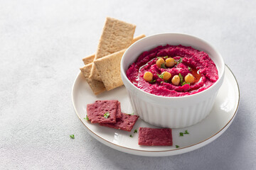 beetroot hummus in white bowl with chickpeas and crackers on gray background. healthy vegetarian eating. close-up. copy space.