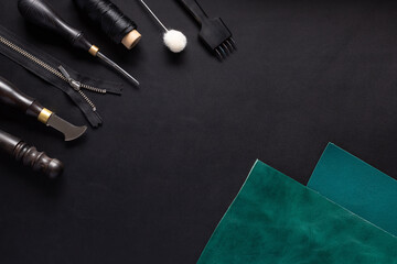 green leather sample and tool kit for handcraft wallets, belts, bags. black leather background. Top view with copy space