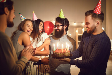 Group of happy young people giving delicious cake to their friend for her birthday